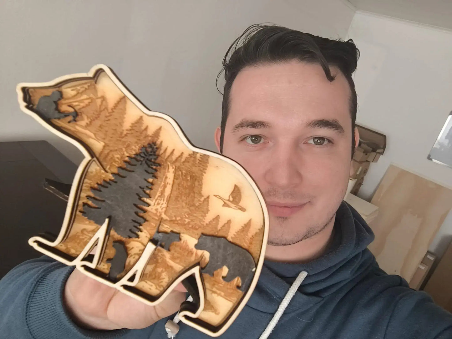 Mann hält 3D Holzdeko Bär in der Hand, kunstvoll mit Bäumen und Tieren gestaltet