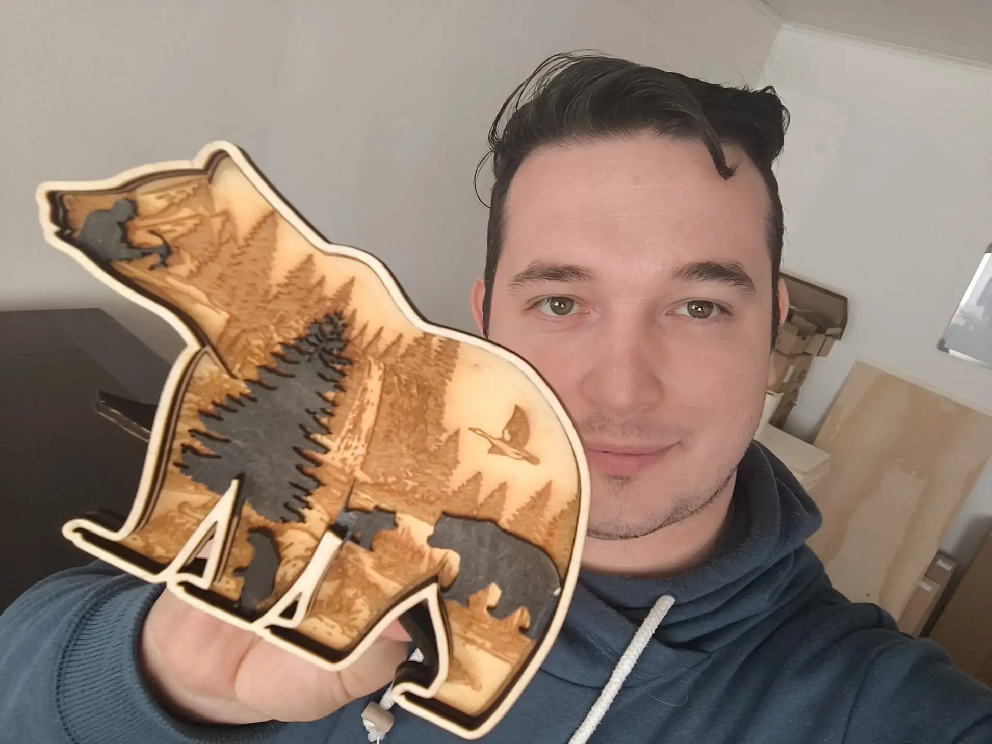 Mann hält 3D Holzdeko Bär in der Hand, kunstvoll mit Bäumen und Tieren gestaltet